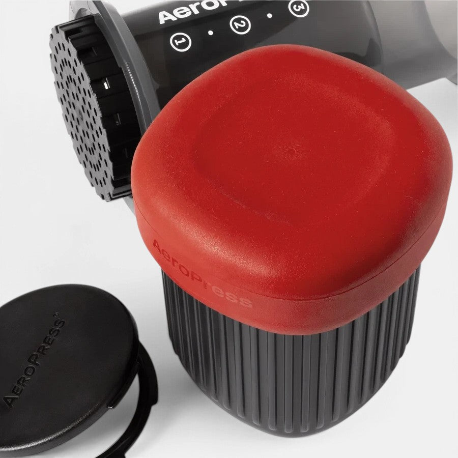 Bootlegger Coffee AeroPress Go portable coffee maker with red lid and black travel mug on a white background