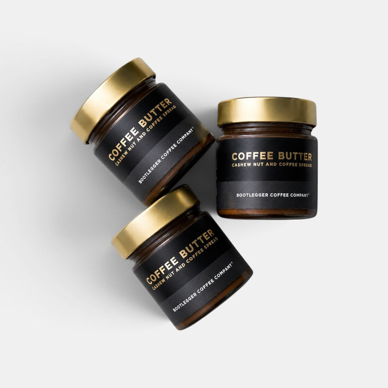 Three glass jars of Bootlegger Coffee Coffee Butter cashew nut and coffee spread with gold lids on white background