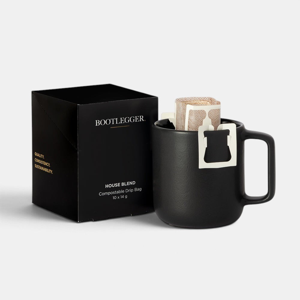 Bootlegger Coffee drip bag brewing in a matte black mug next to a black box of compostable coffee drip bags.